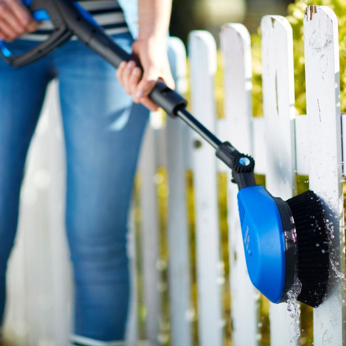 Rotating brush with flexible hose for high-pressure cleaners being used to clean a white wooden fence.
