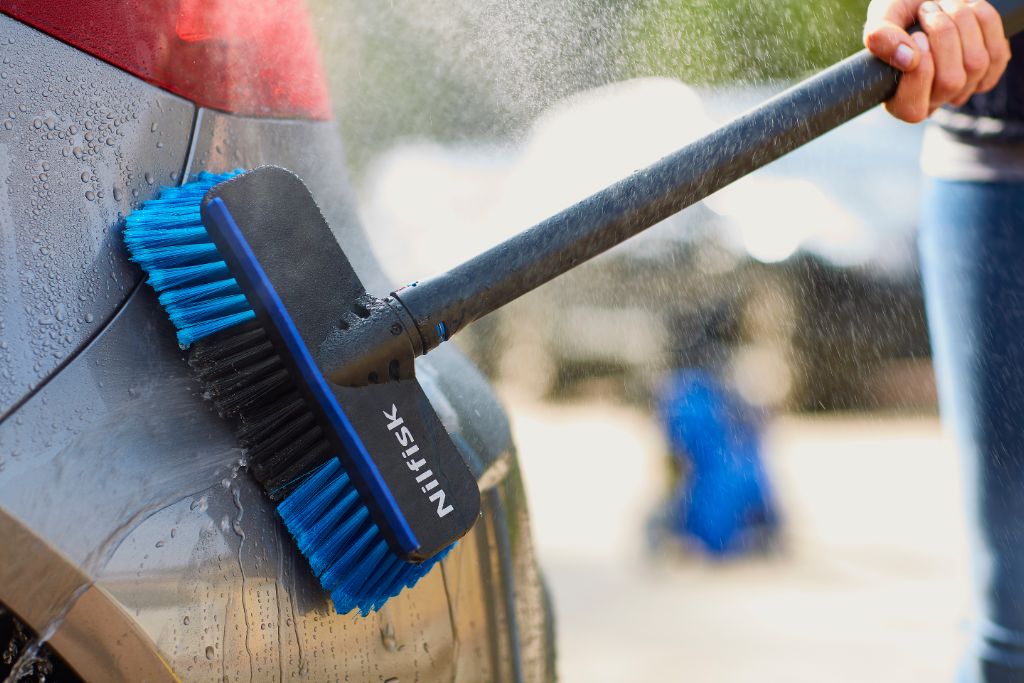 Blue and black car washing brush by Nilfisk being used to clean a gray car.