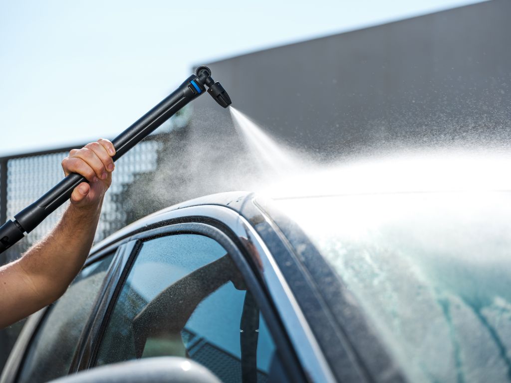 Pressure washer undercarriage nozzle for high-pressure cleaners with a black wand spraying water onto a car.