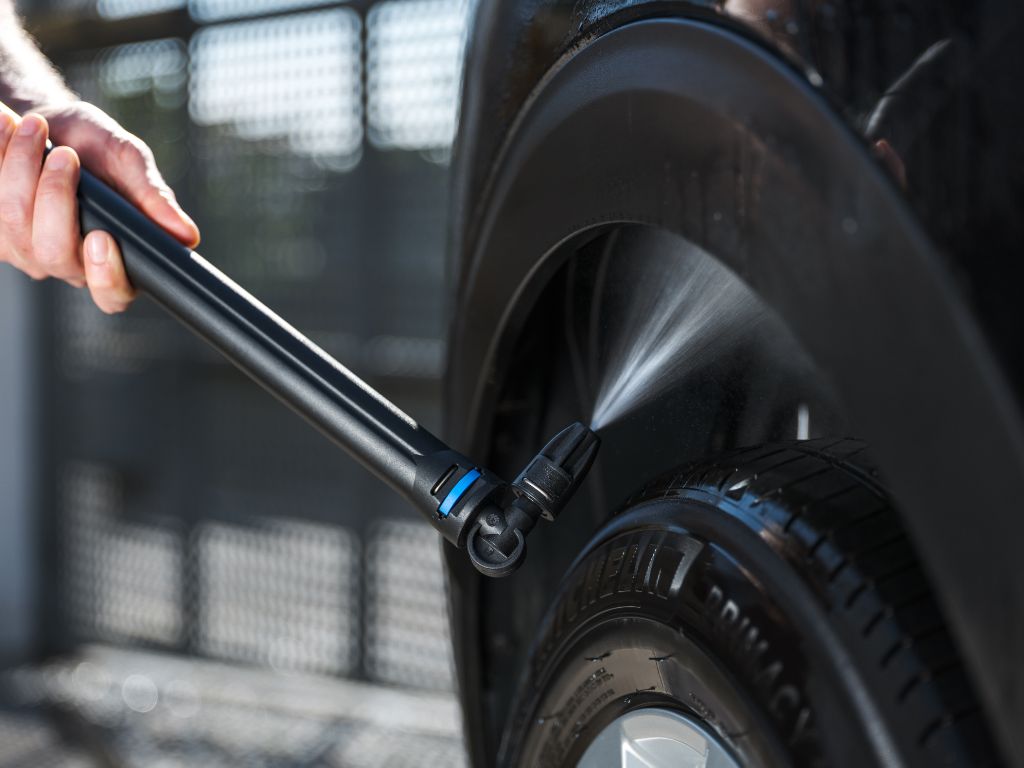 Undercarriage nozzle for pressure washers by ES, cleaning a car tire with a jet of water.