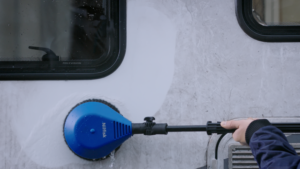 Blue rotating brush for pressure washers by Nilfisk being used on a windowed surface.
