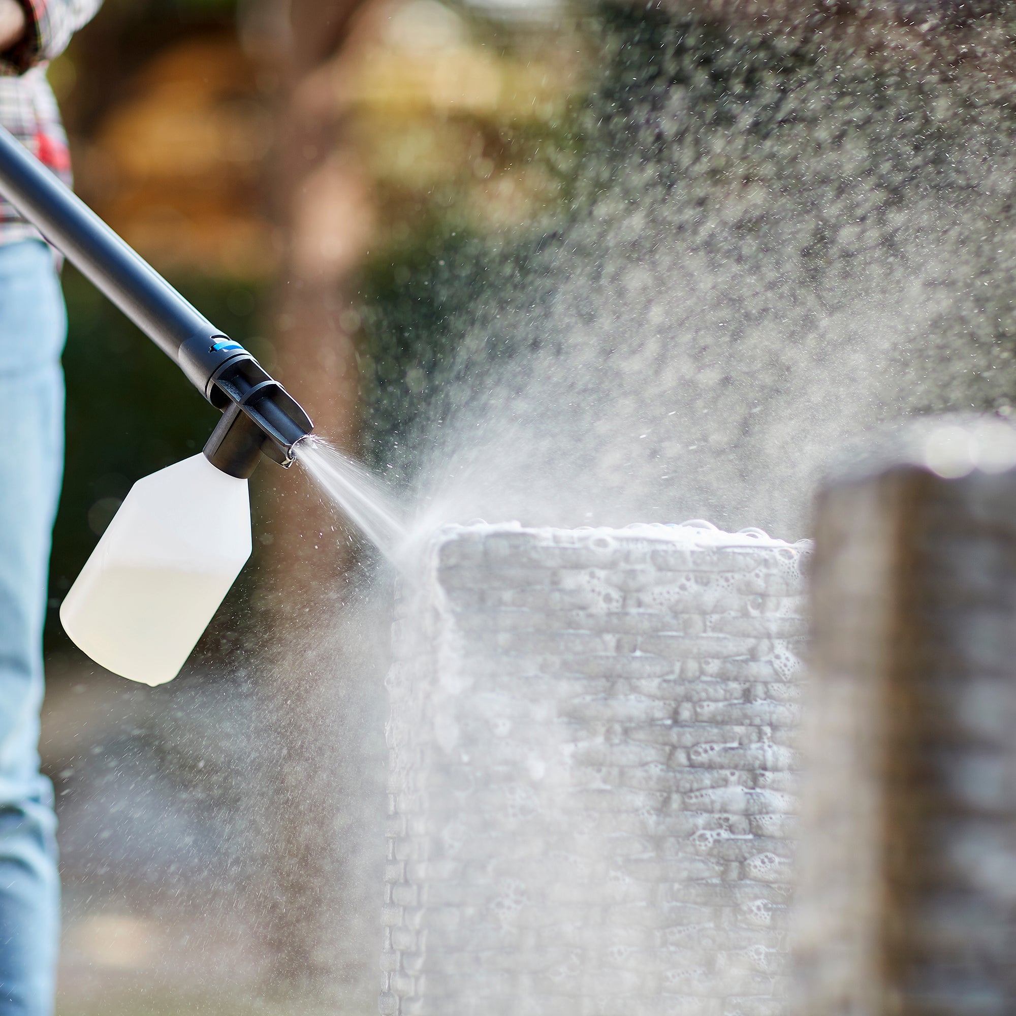 High-pressure cleaner for car washing by C 110.7-5 X-TRA, with soap sprayer attached, being used by person in plaid shirt and jeans.
