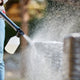 High-pressure cleaner for car washing by C 110.7-5 X-TRA, with soap sprayer attached, being used by person in plaid shirt and jeans.
