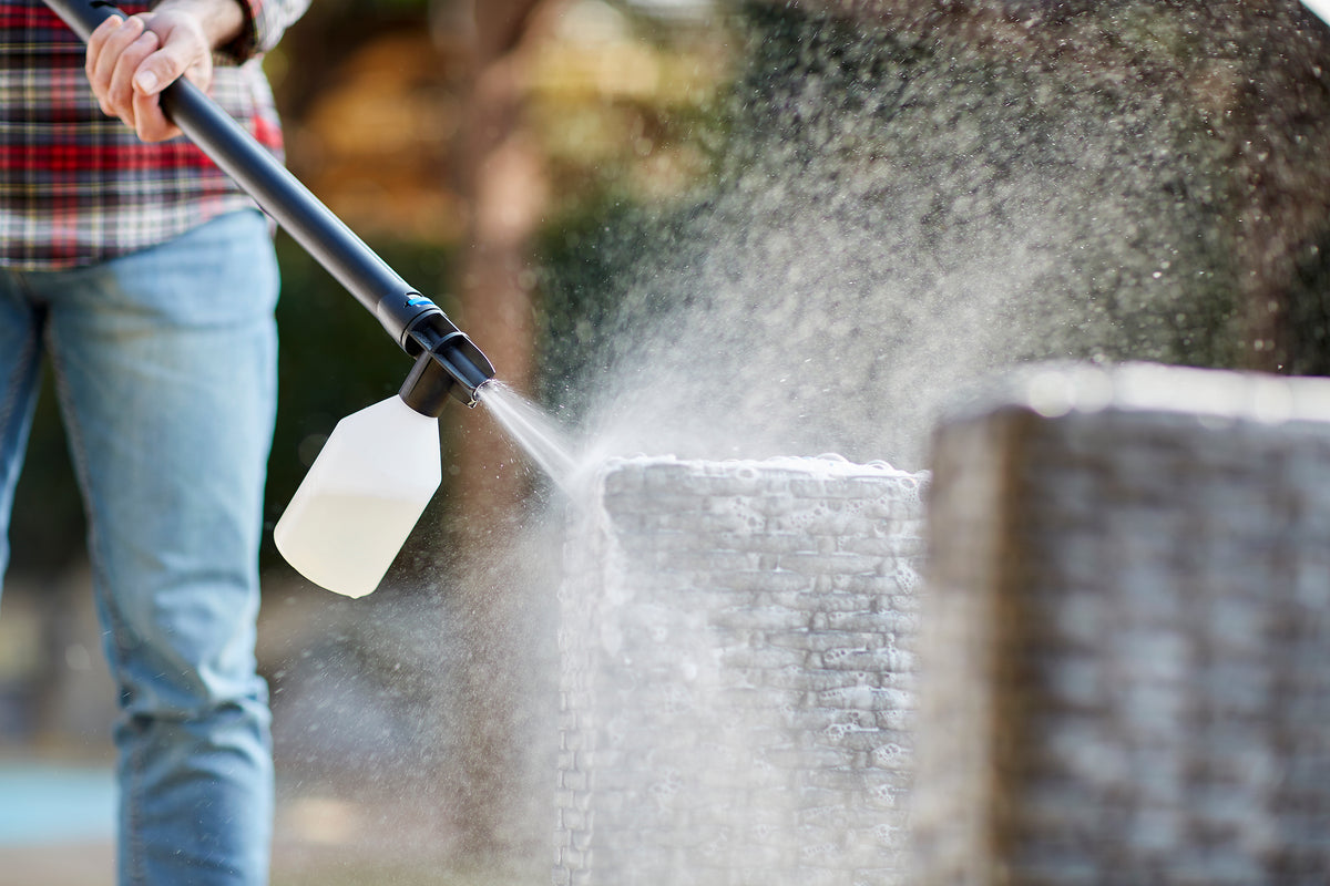 High-pressure cleaner for car washing by C 110.7-5 X-TRA, with soap sprayer attached, being used by person in plaid shirt and jeans.
