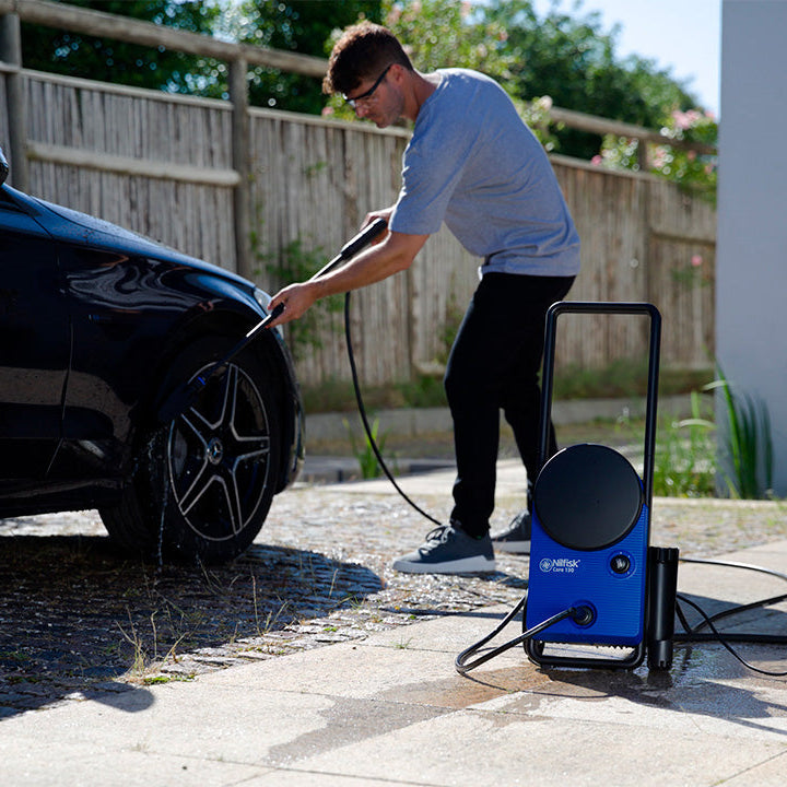 Blue pressure washer by Nilfisk, seen with its black handle and being used to wash a dark car.
