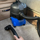 Blue wet/dry vacuum by Nilfisk with a black hose and cleaning head on a carpeted floor.
