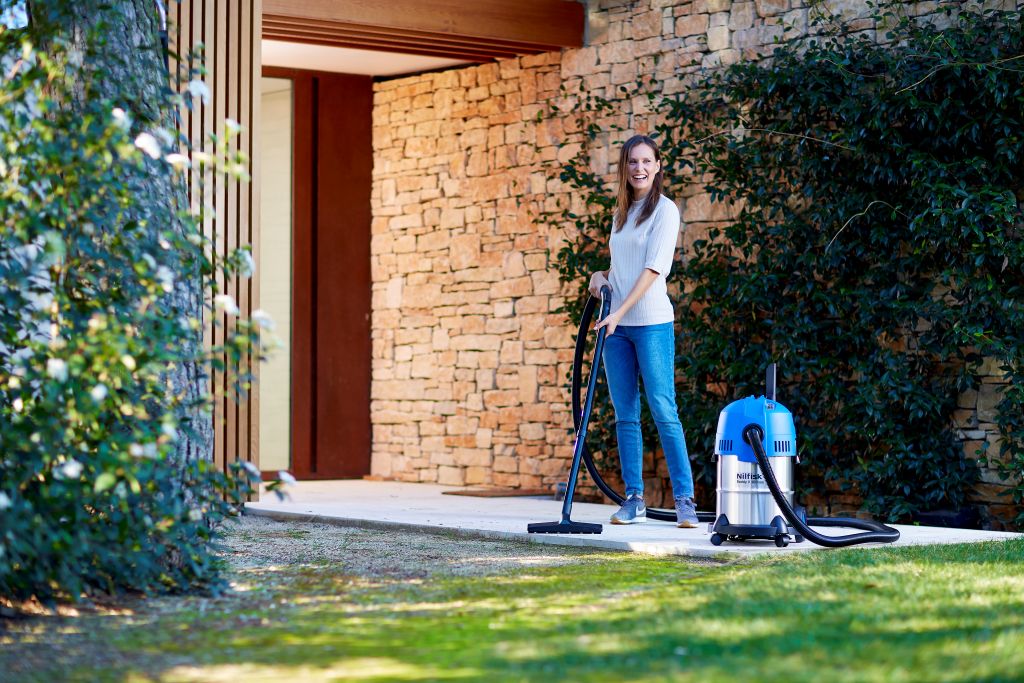 Blue and silver wet/dry vacuum by Nilfisk, used by a woman standing on a patio.
