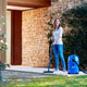 Blue wet and dry vacuum cleaner by Nilfisk, with a woman using the tool near the house.