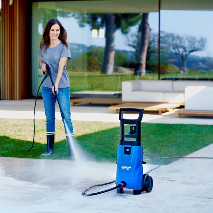Blue pressure washer by Nilfisk being used to clean an outdoor patio, with a woman operating the spray nozzle.