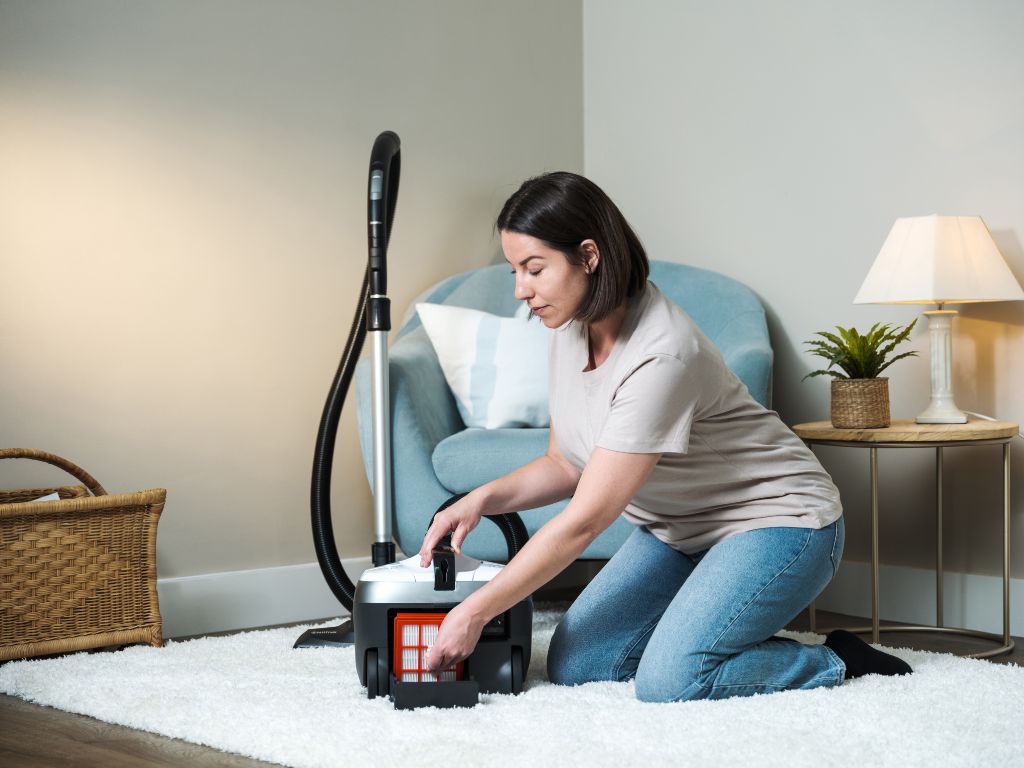 White vacuum cleaner, 650 W, beside a woman on a white rug in a living room setting.