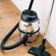 Silver canister vacuum cleaner by Nilfisk with a black hose and cleaning head on a hardwood floor.
