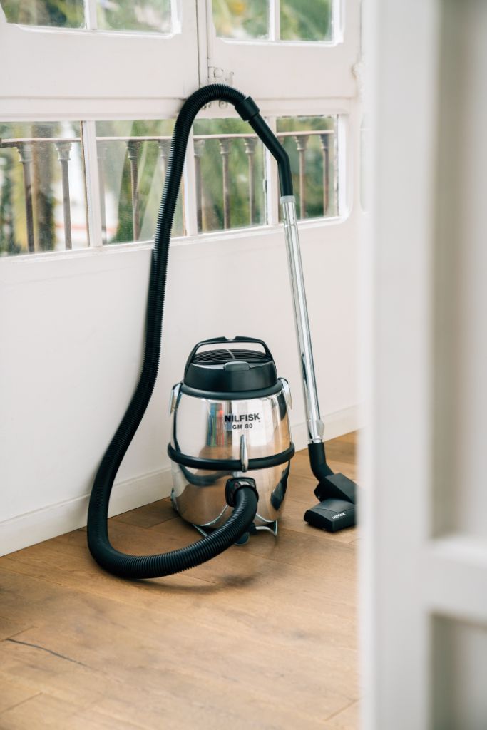 Silver canister vacuum cleaner from Nilfisk with a black hose and chrome wand, standing on a wooden floor.