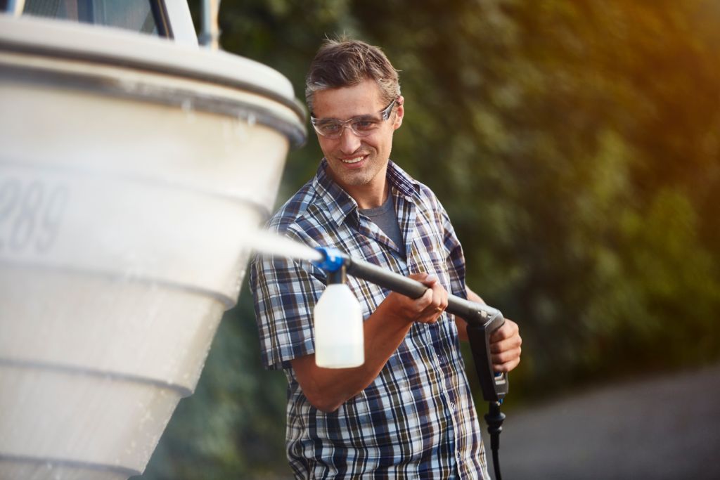 Pressure washer cleaner by ES, used on a boat, with a man wearing a plaid shirt.
