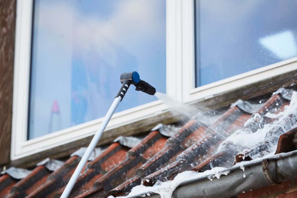 High-pressure washer nozzle spraying foam on algae-stained red roof tiles, side view, lifestyle use