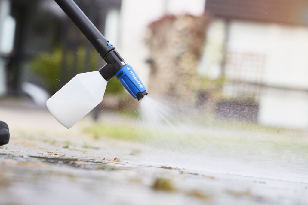 Foam sprayer for pressure washers by Nilfisk spraying water onto a surface outdoors.