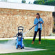 Blue pressure washer by Nilfisk in a yard, with woman in denim shirt operating it.
