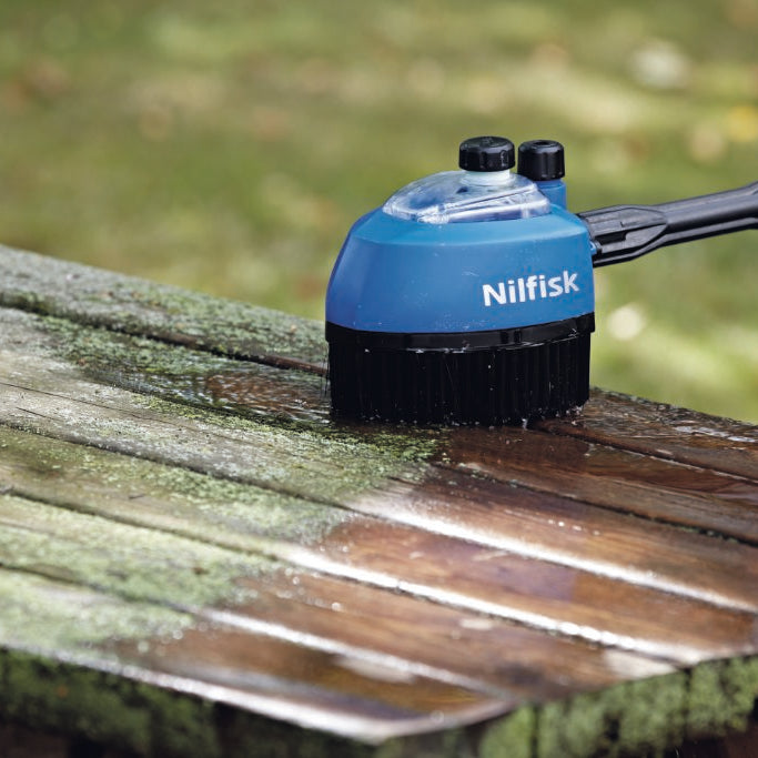 Rotary brush head for pressure washer by Nilfisk cleaning a wooden table outdoors.
