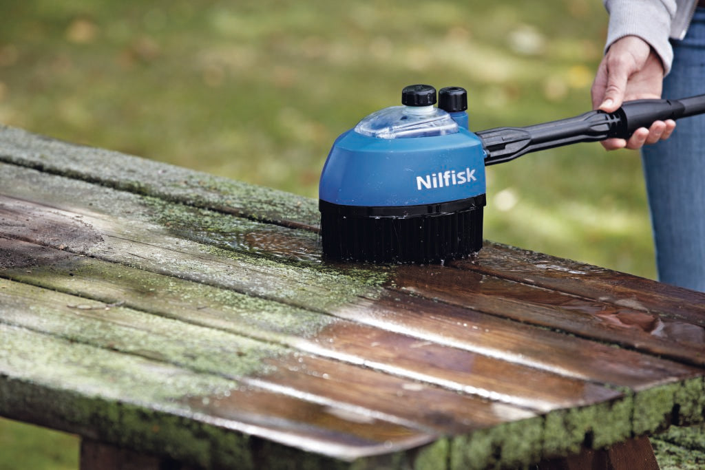 Rotary brush head for pressure washer by Nilfisk cleaning a wooden table outdoors.