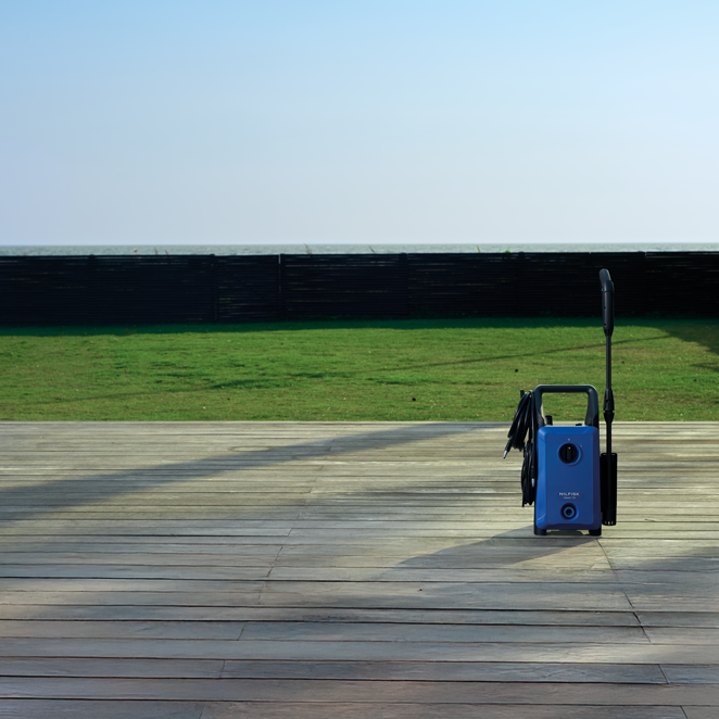 Blue high-pressure washer with black handle and hose, positioned on wooden deck, outdoor lifestyle view