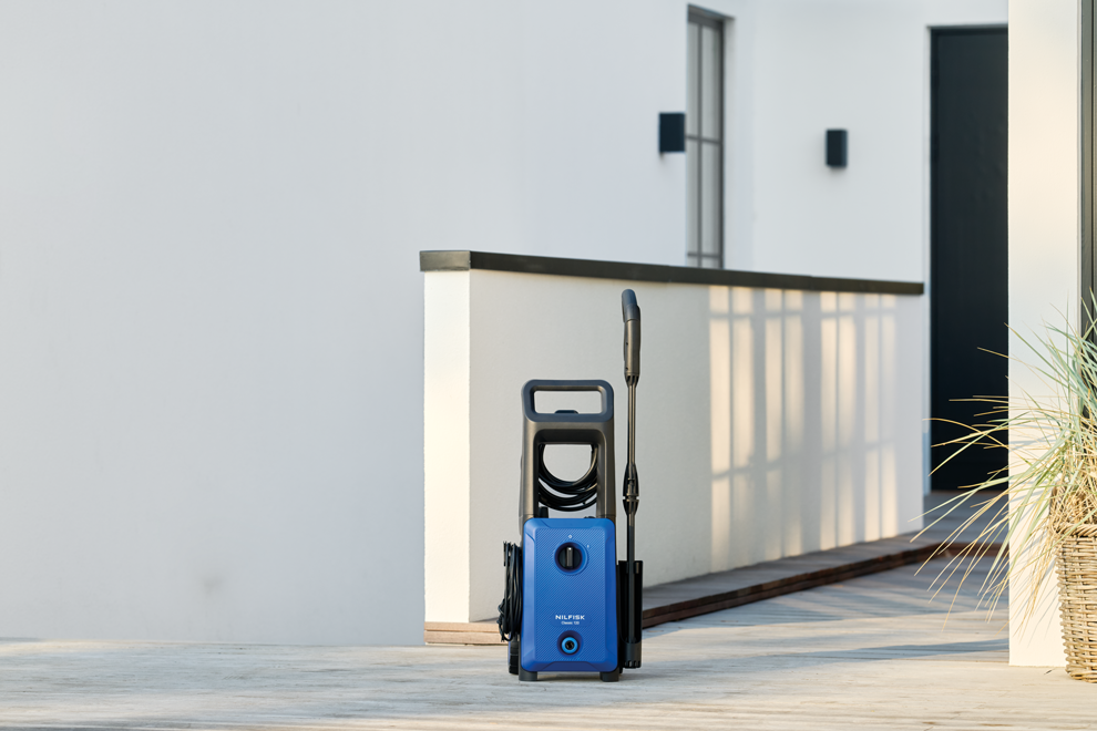 Blue and gray high-pressure washer with black hose and spray wand, by Nilfisk, on outdoor patio, front view, modern design