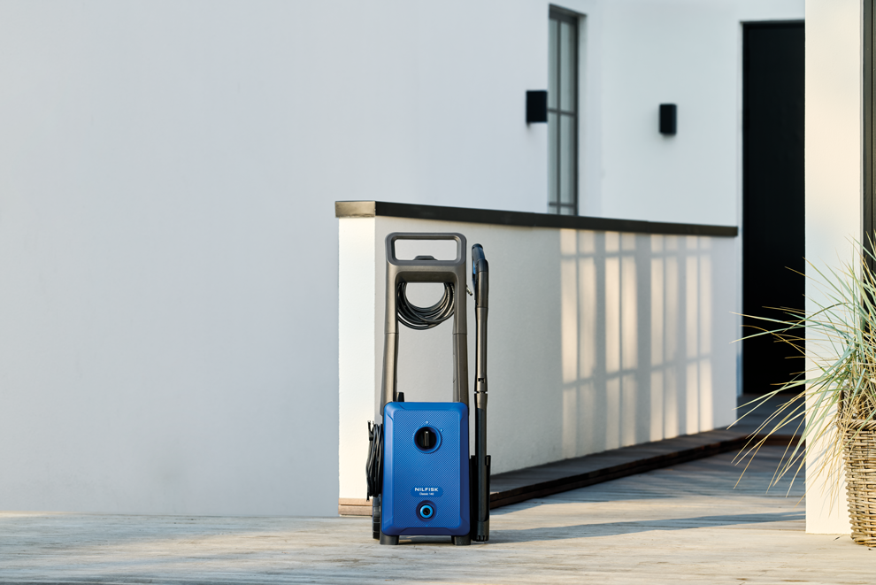 Blue and gray high-pressure washer with coiled hose and spray wand, by Nilfisk, on outdoor patio, side view