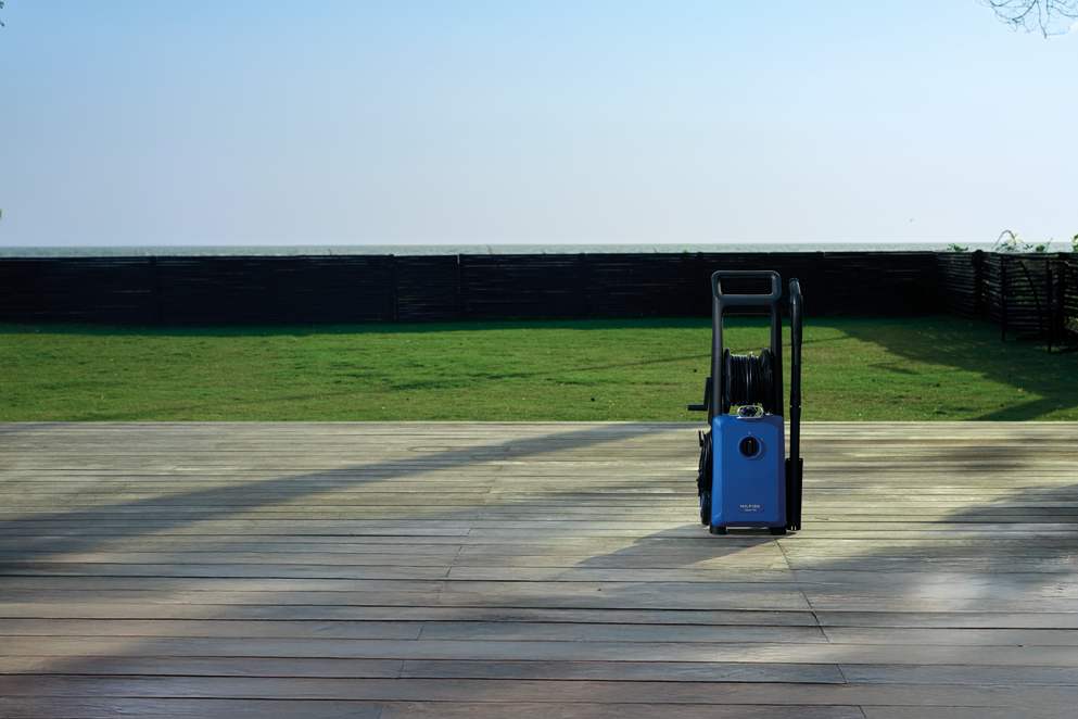 Blue high-pressure washer with black handle and hose reel, on wooden deck, side view, outdoor setting