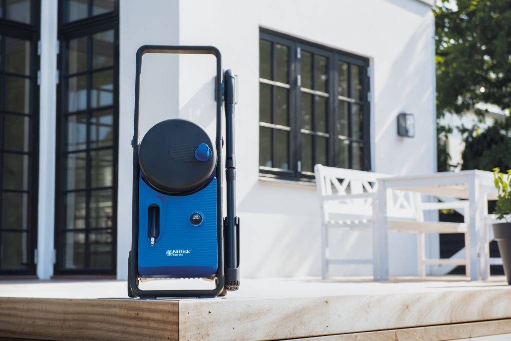 Blue and black high-pressure washer with circular top and textured body by Nilfisk, positioned on wooden deck outdoors, side view.