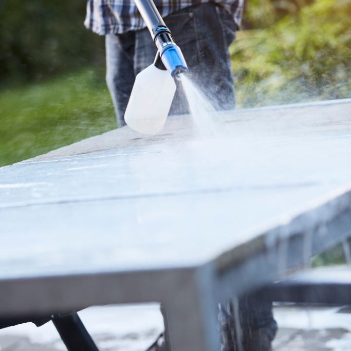 Stone sealer by ES being sprayed onto stone surface, with visible plaid shirt and jeans.