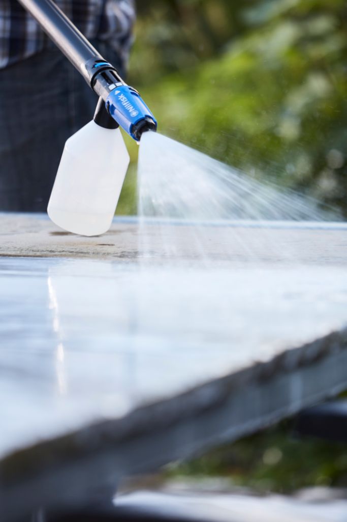 Pressure washer cleaner by Nilfisk spraying onto a stone surface with visible reflections.
