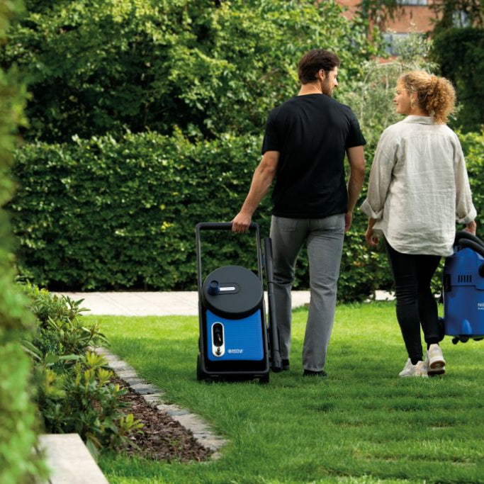 Blue high-pressure washer by Nilfisk, on a cart with a hose reel, outdoors in a garden.