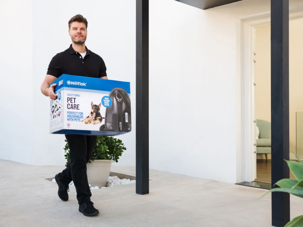 Black pet care vacuum cleaner by Nilfisk in box, held by man in modern home, lifestyle view