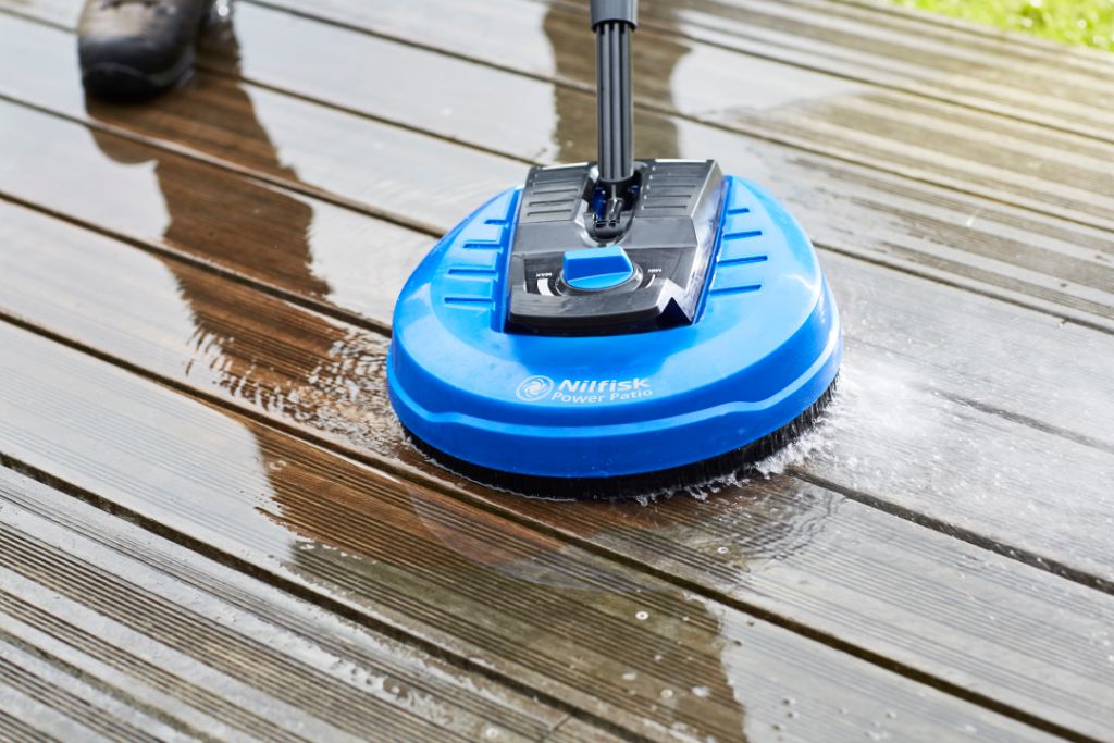 Blue power patio cleaner by Nilfisk cleaning a wooden deck with water spraying.