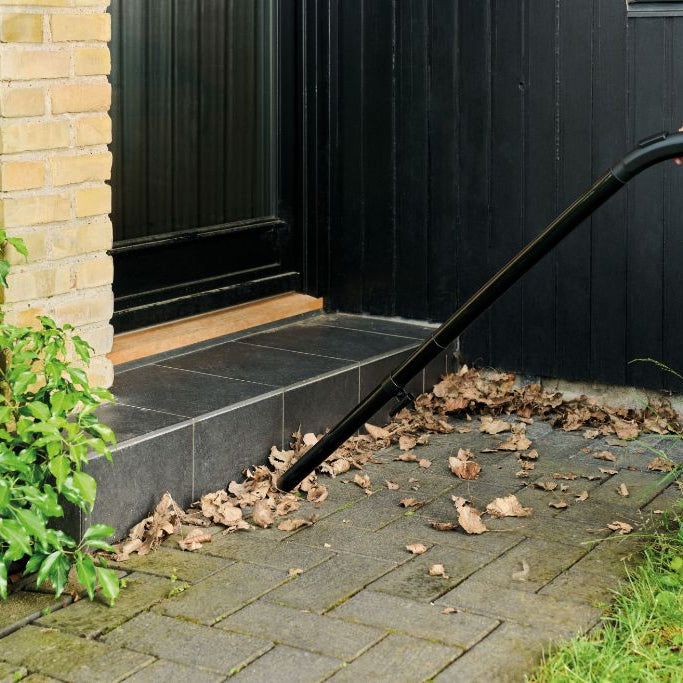 Wet/dry vacuum with floor nozzle by Nilfisk, cleaning up leaves near a doorstep.