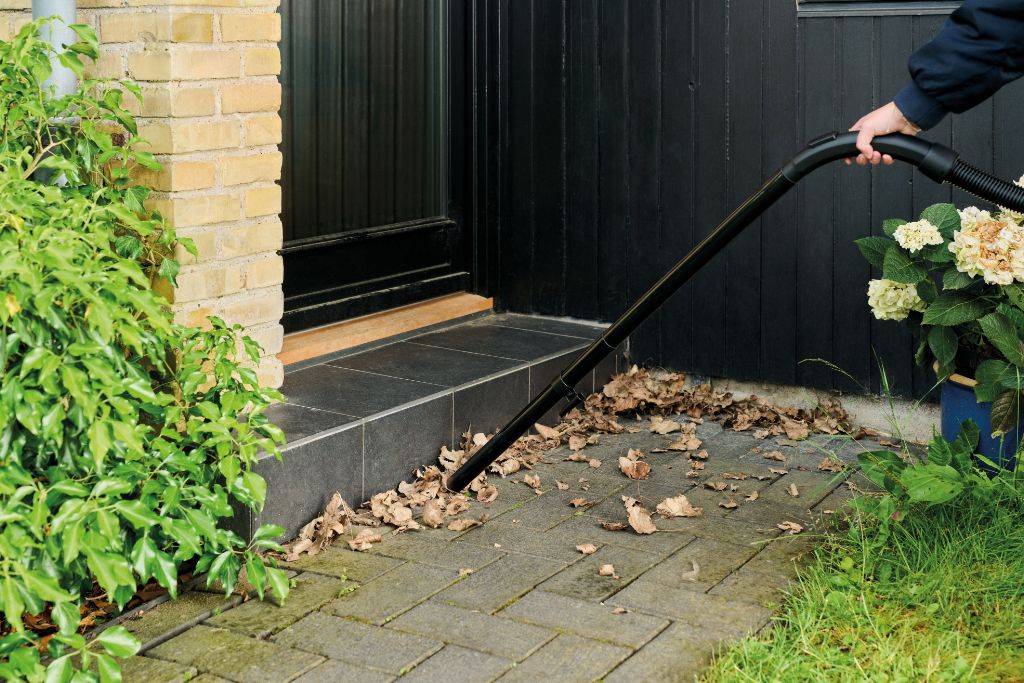 Wet/dry vacuum with floor nozzle by Nilfisk, cleaning up leaves near a doorstep.
