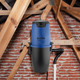 Blue and black central vacuum cleaner by Nilfisk with the hose running down out of view, in an attic.