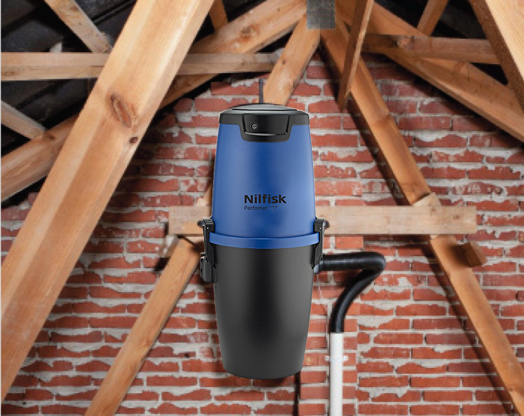 Blue and black central vacuum cleaner by Nilfisk with the hose running down out of view, in an attic.