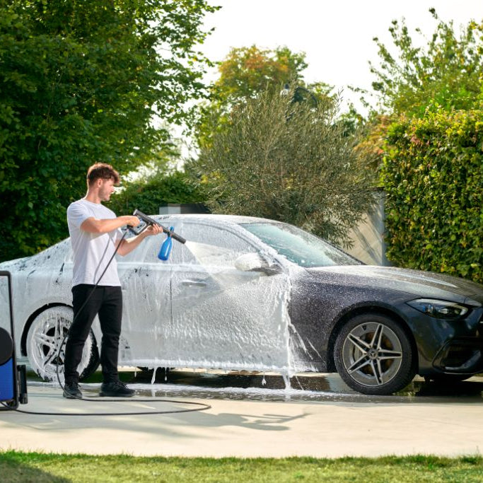 High-pressure washer with multifunction car wash nozzle by Nilfisk, next to a foamed-up car.