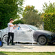 High-pressure washer with multifunction car wash nozzle by Nilfisk, next to a foamed-up car.