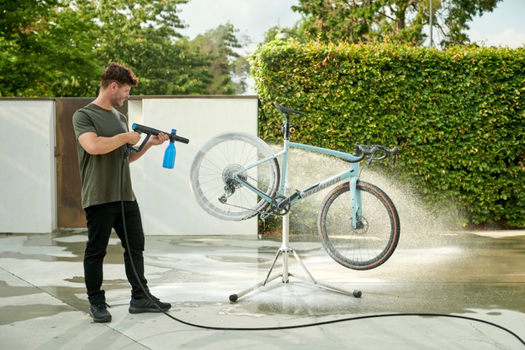Højtryksrenser med multifunktionsdyse by Nilfisk in use for washing a light blue bicycle.
