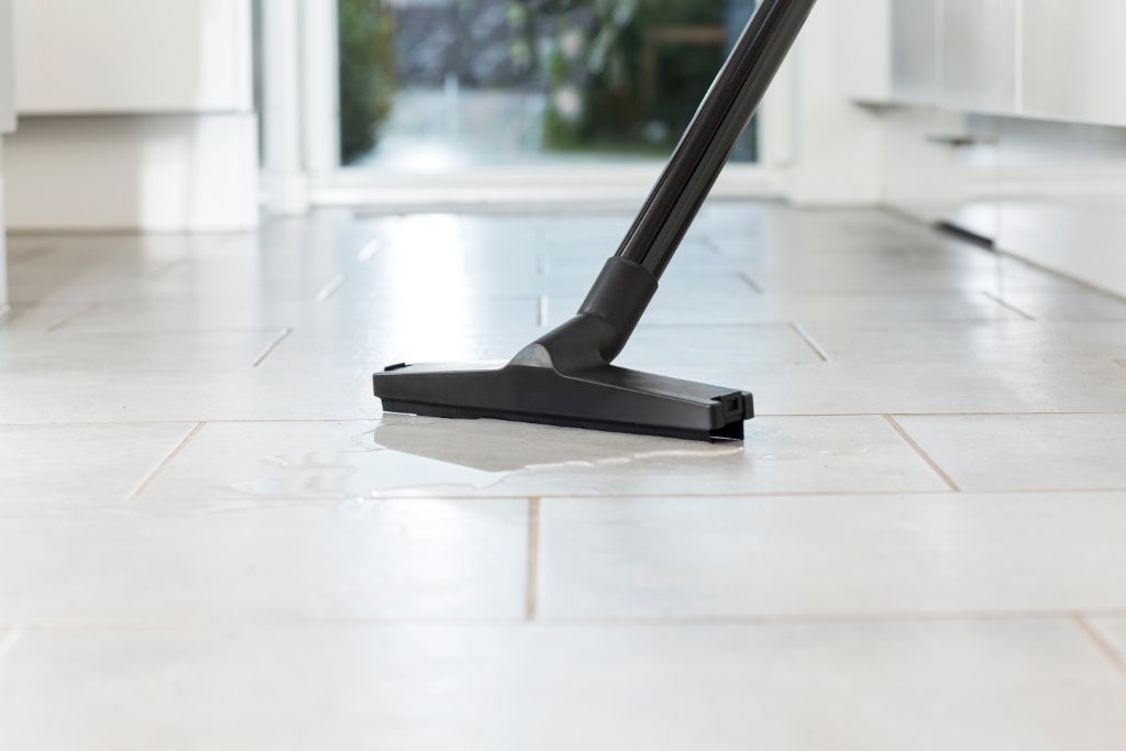 Wet/dry vacuum cleaner with floor nozzle by Nilfisk, cleaning a tiled floor surface with water.
